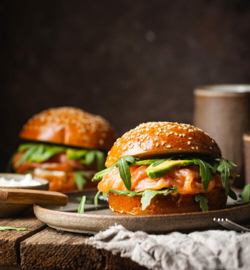 Burger sandwich with salmon, cream cheese, avocado and arugula on a light background, concept diet food, take away, healthy fast food