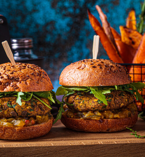 Vegan lentil burger with arugula, mustard sauce, fresh vegetables and sweet potato fries on a wooden board. Vegan food concept.